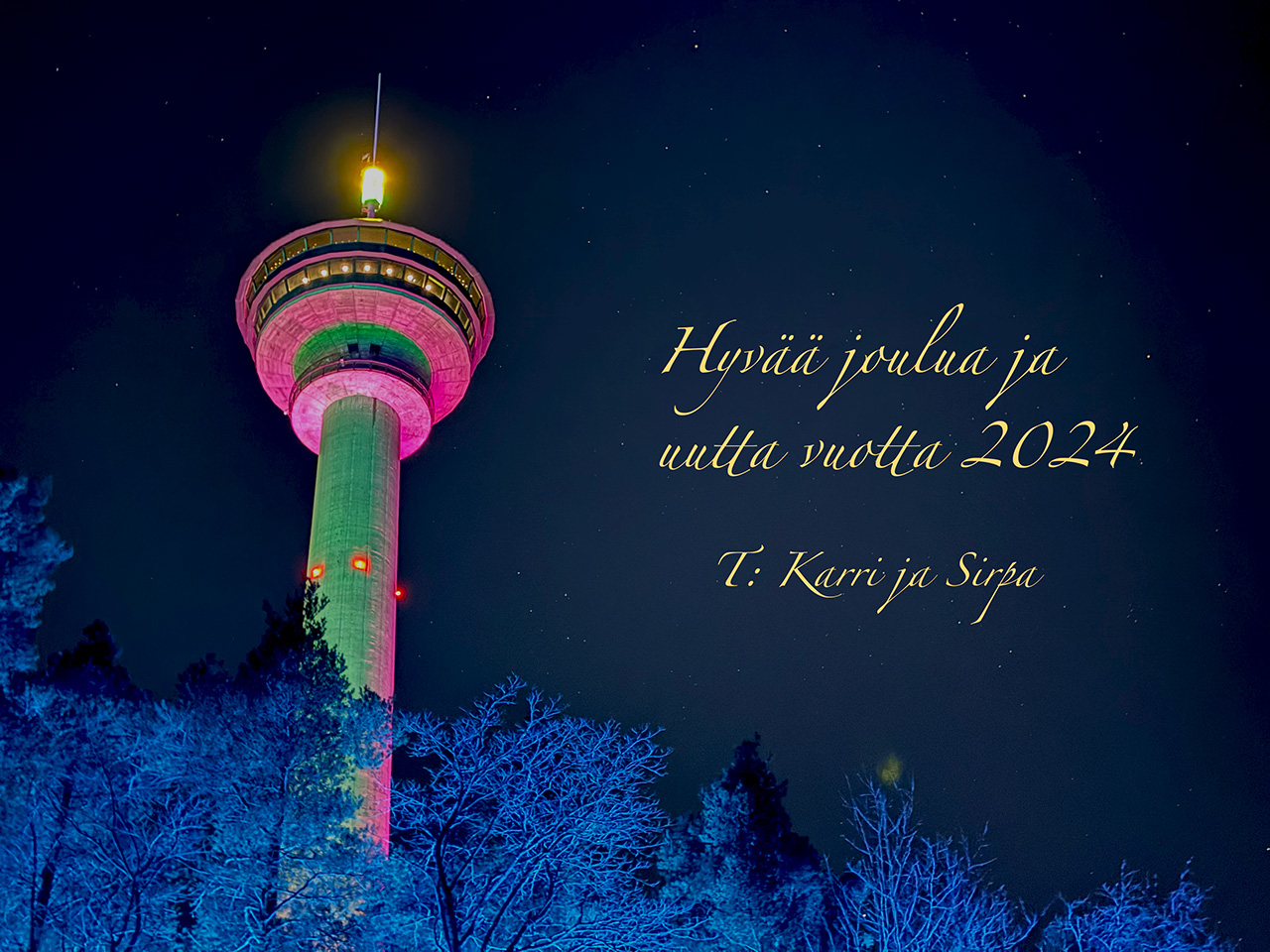 The Näsinneula tower in Tampere lit with red lights, seen from the below with snowy tree tops lit with blue lights in front. On the right side of the tower a greeting Hyvää joulua ja uutta vuotta 2024 from Karri and Sirpa. A full size photo is available with a click.